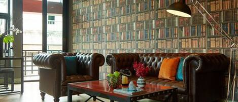A living room with a leather sofa, a coffee table, and a bookshelf in the background.