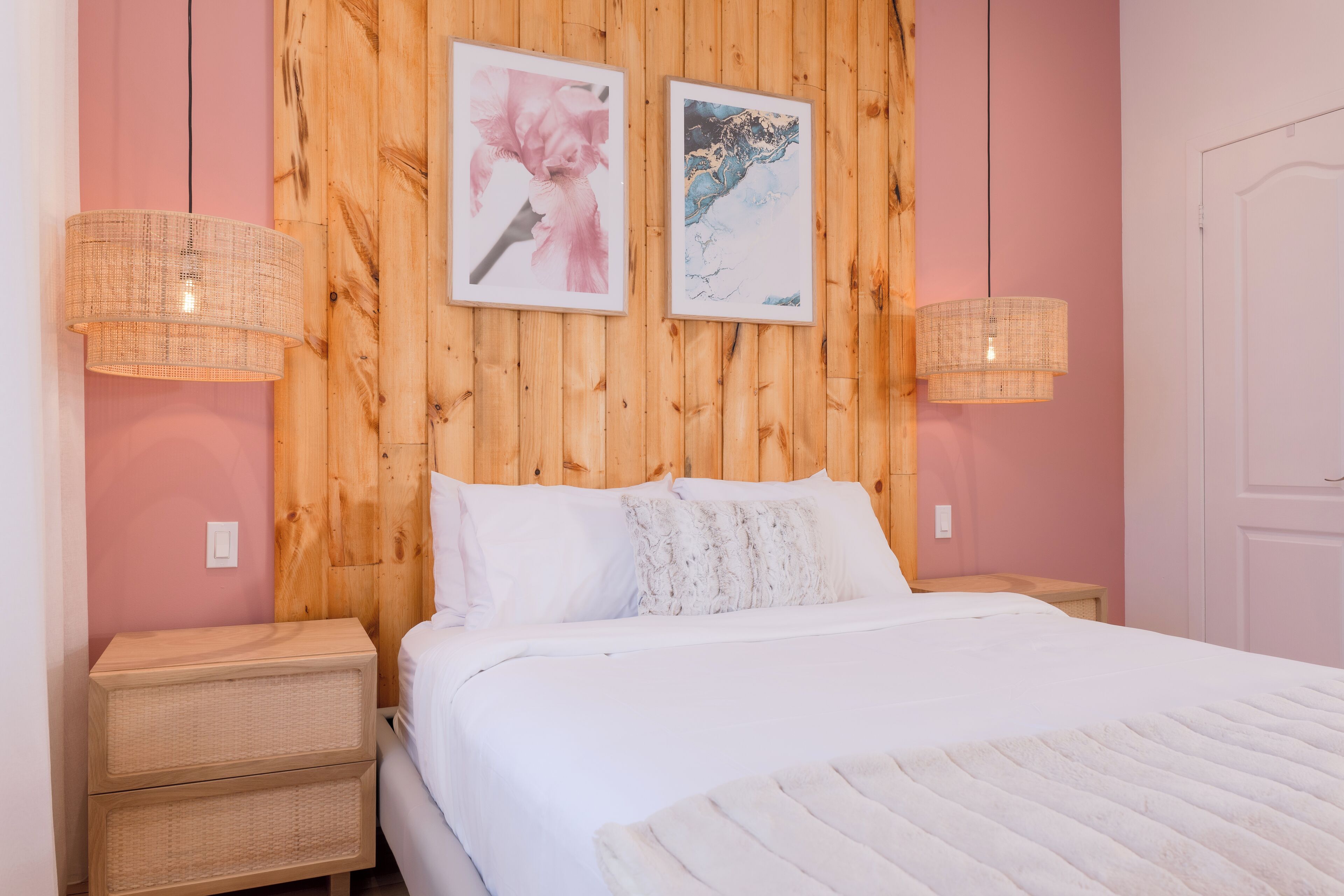 A bedroom with a wooden headboard, two wall-mounted lamps, a bed with white bedding, and two nightstands with wicker drawers.