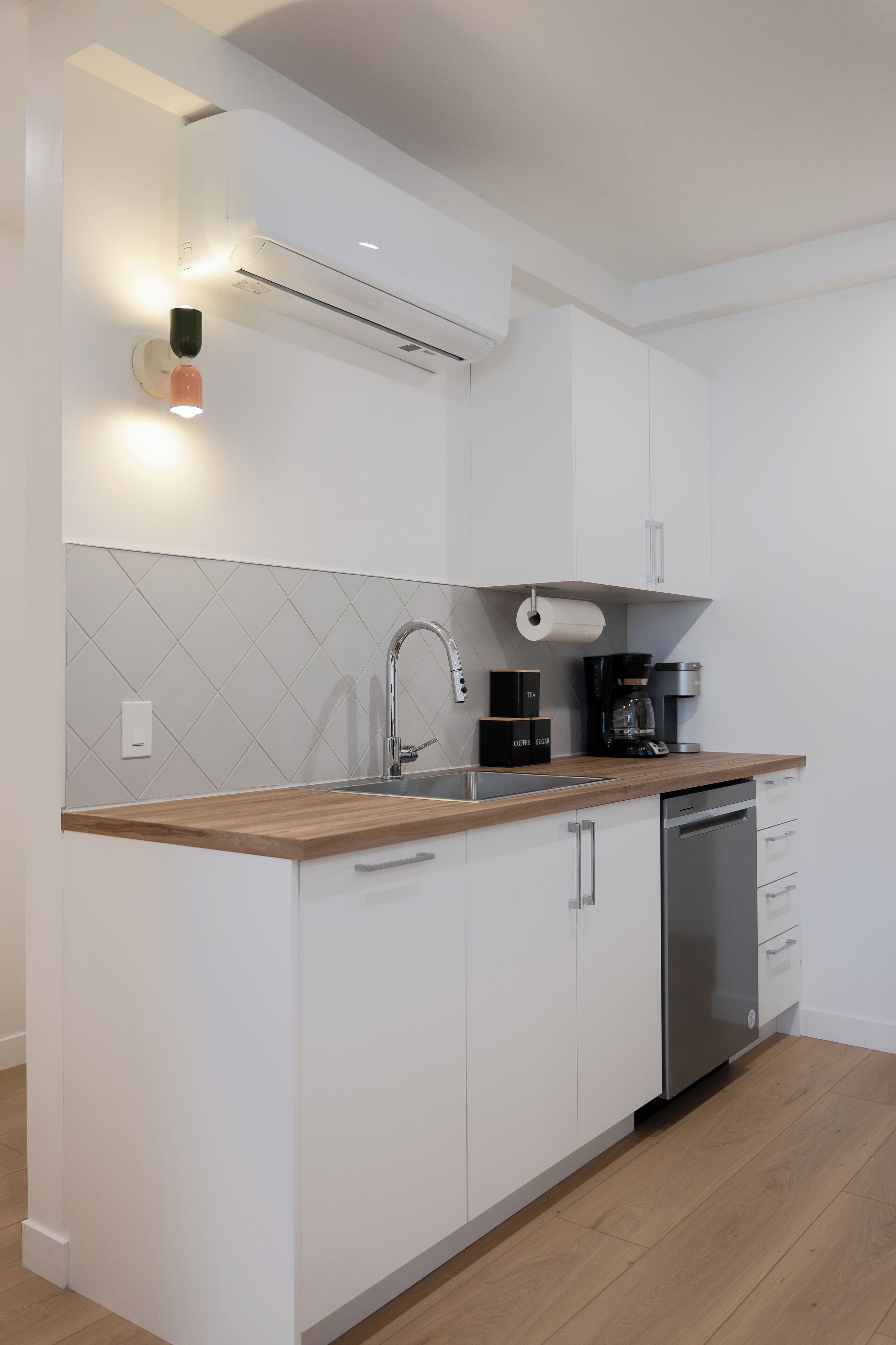 A modern kitchen with white cabinetry, a wooden countertop, a stainless steel dishwasher, and a coffee maker.