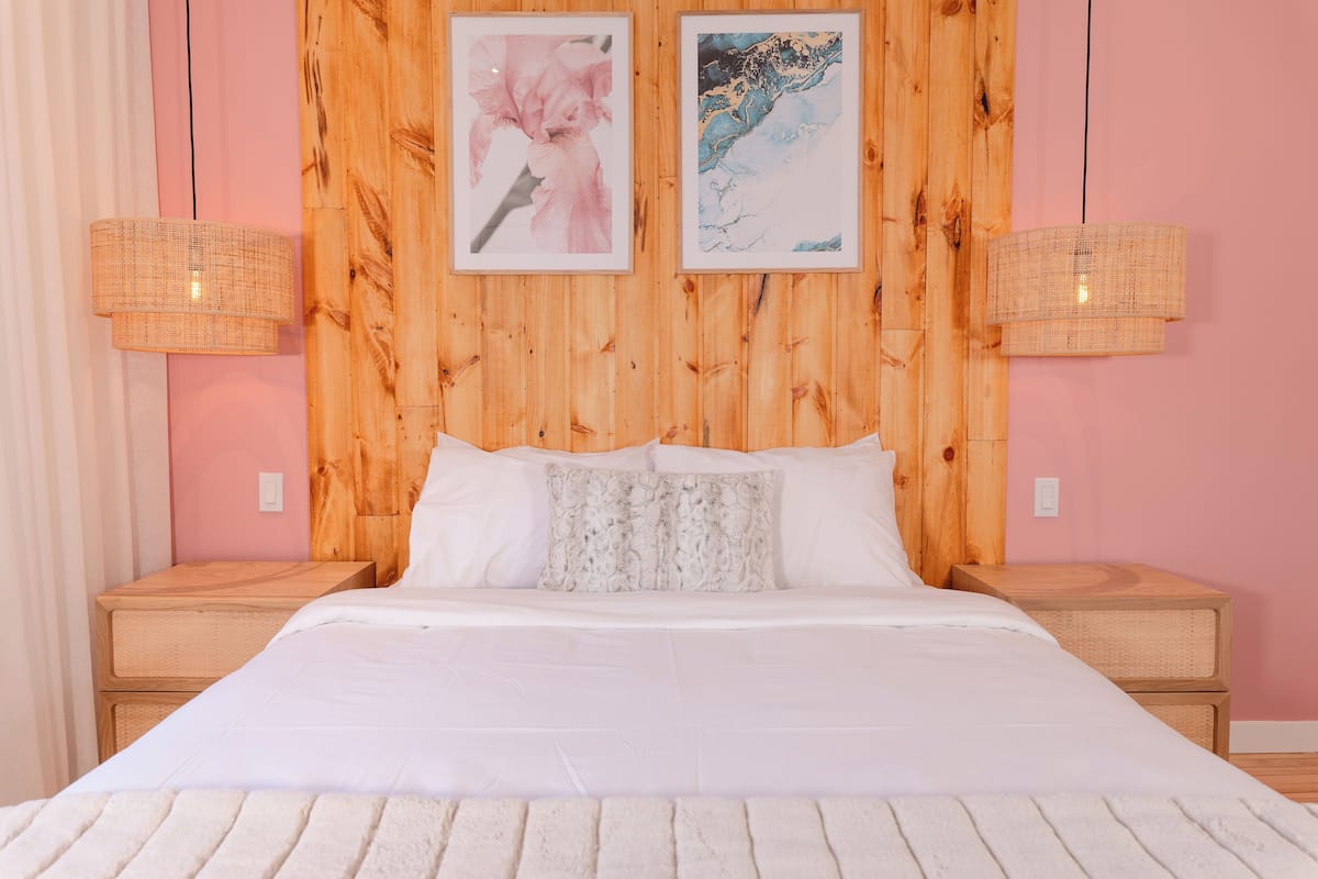 Un dormitorio con cabecera de madera, dos mesitas de noche, una cama con ropa de cama blanca y dos lámparas de pared.