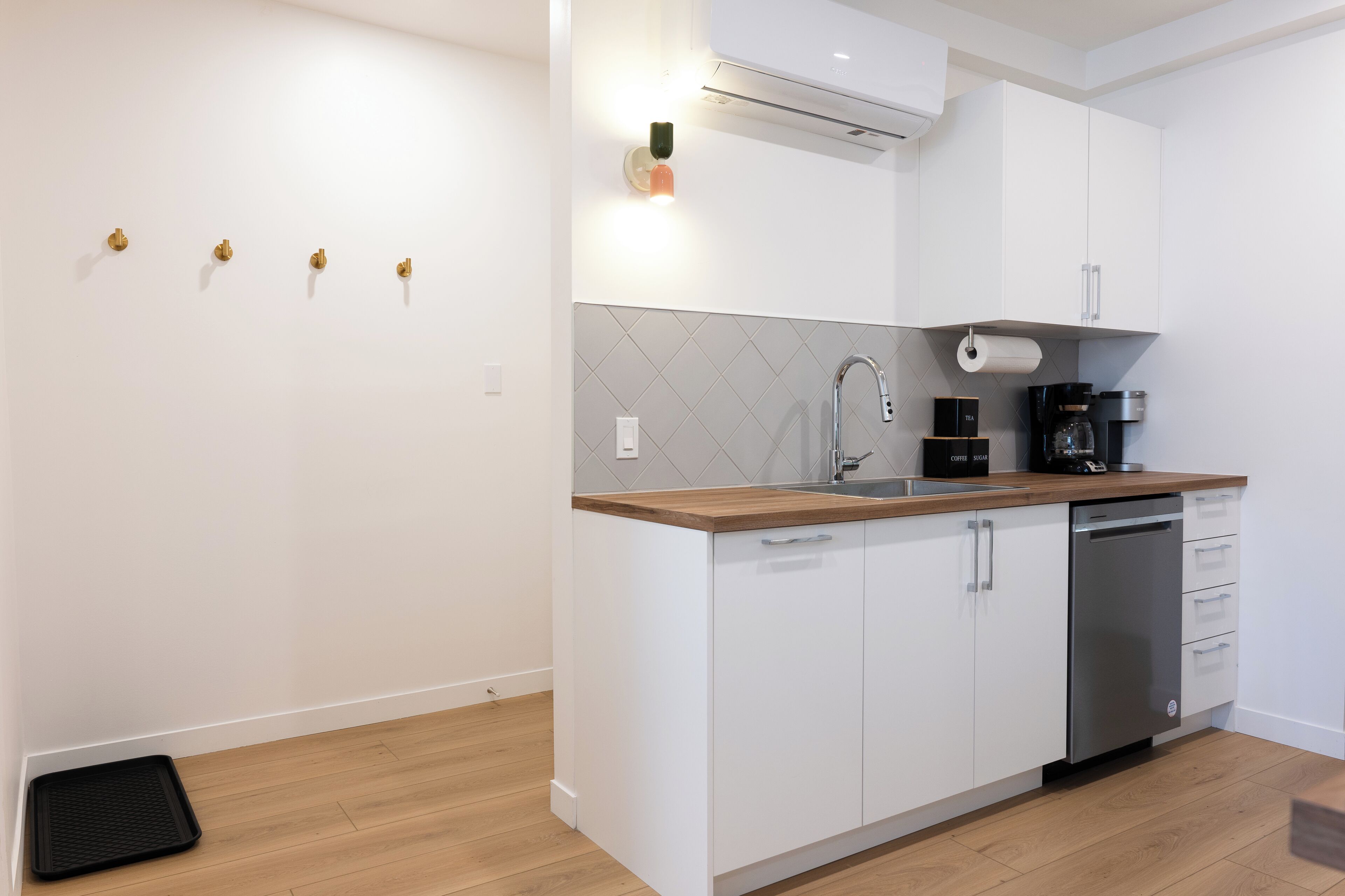 A modern kitchen with white cabinets, a wooden countertop, a stainless steel dishwasher, and a built-in oven.