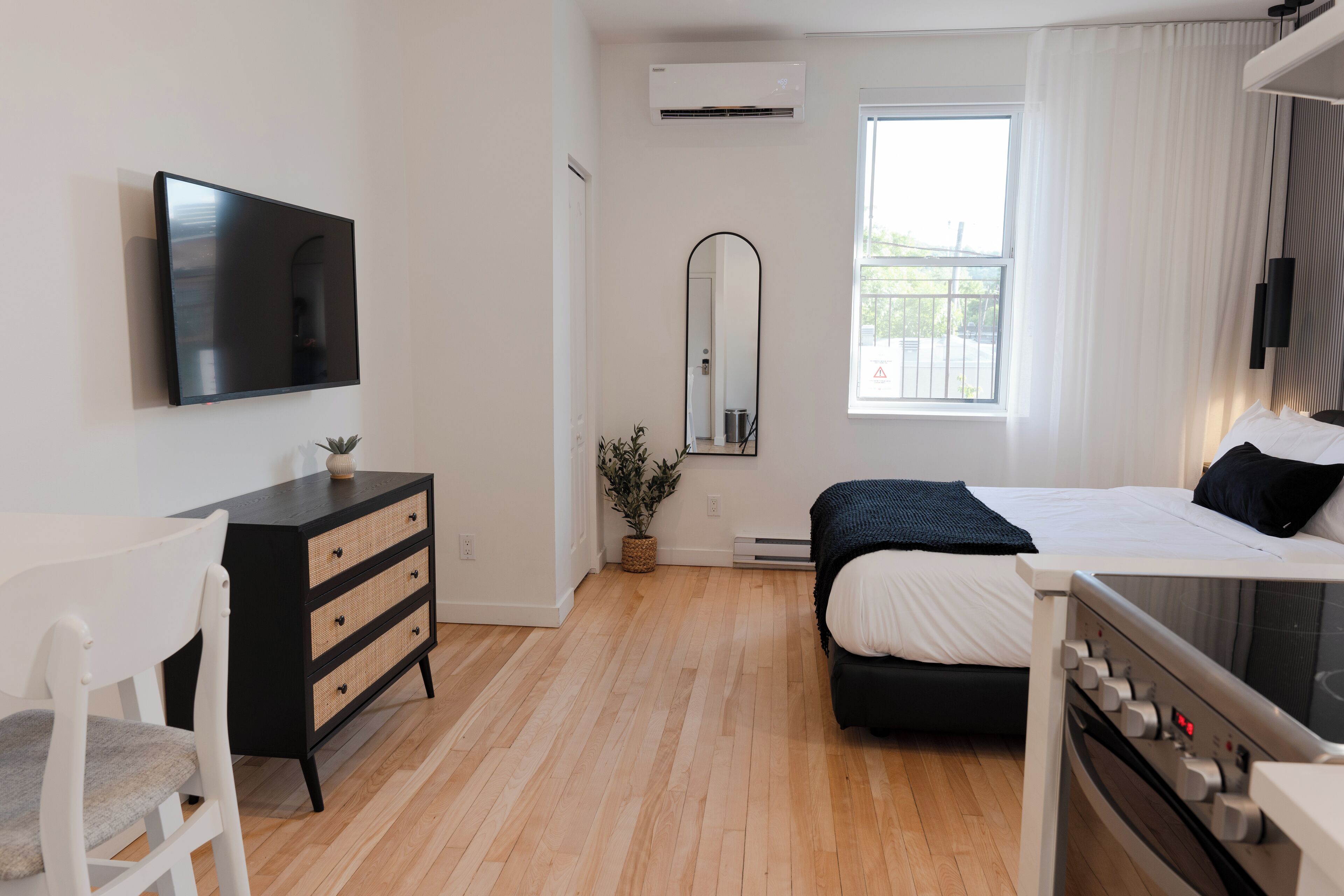 A modern bedroom with a bed, a TV, a dresser, and a window with curtains.