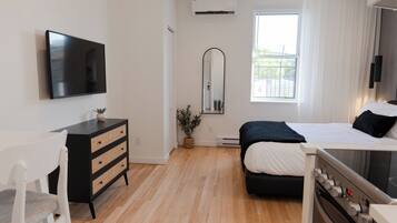 A modern bedroom with a bed, a TV, a dresser, and a window with curtains.