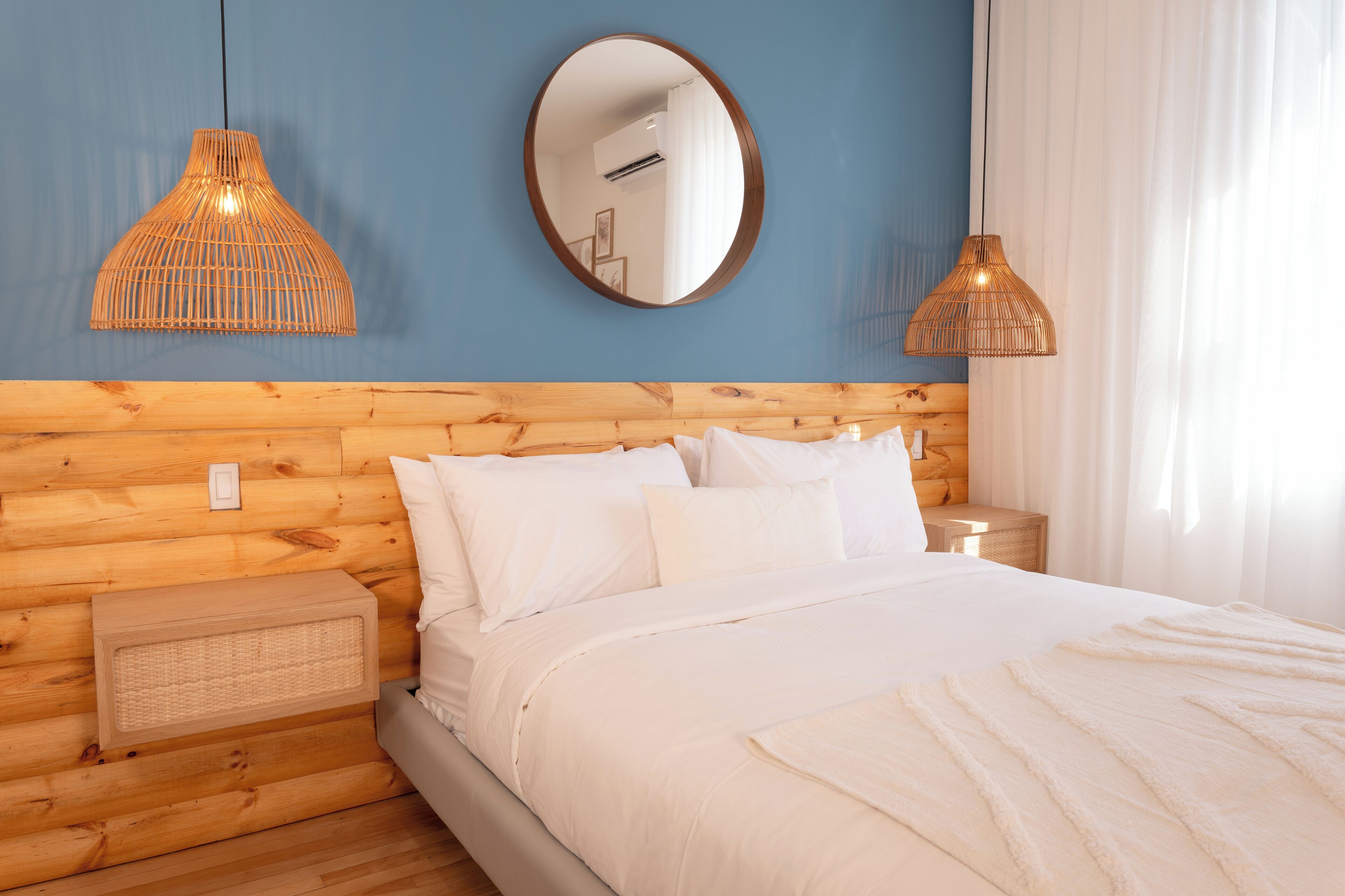 A neatly made bed with white linens, a wooden headboard, and two wall-mounted pendant lights.