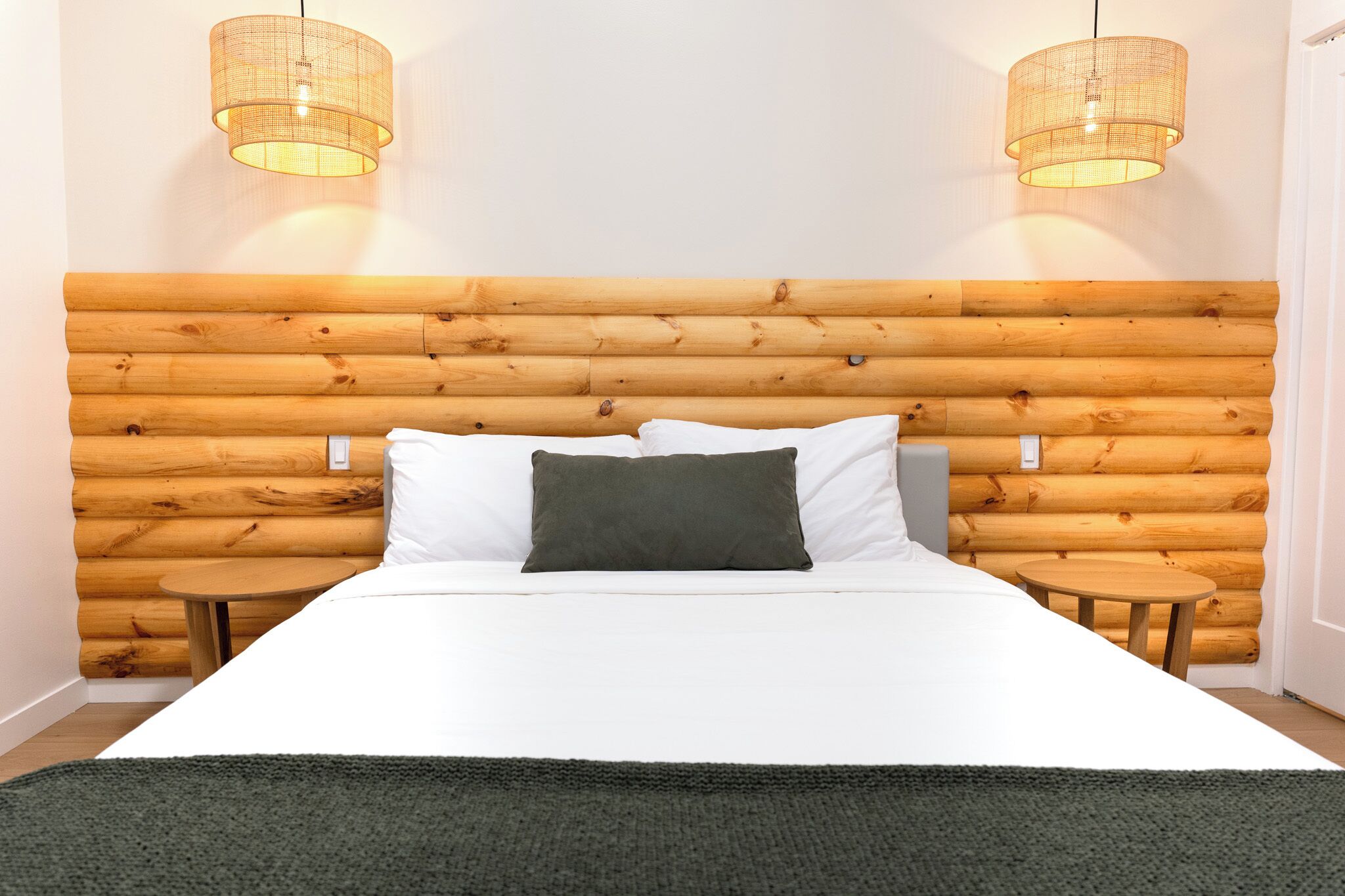 Une chambre à coucher avec une tête de lit en bois brut, du linge de lit blanc, deux tables de chevet et deux lampes en osier.