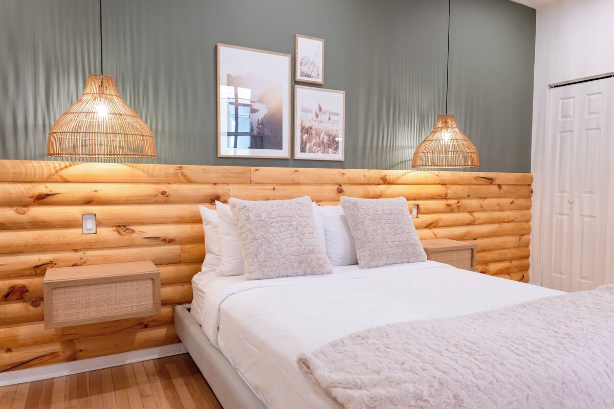Un dormitorio de estilo cabaña con cabecera de madera, ropa de cama blanca y dos lámparas fijadas a la pared.