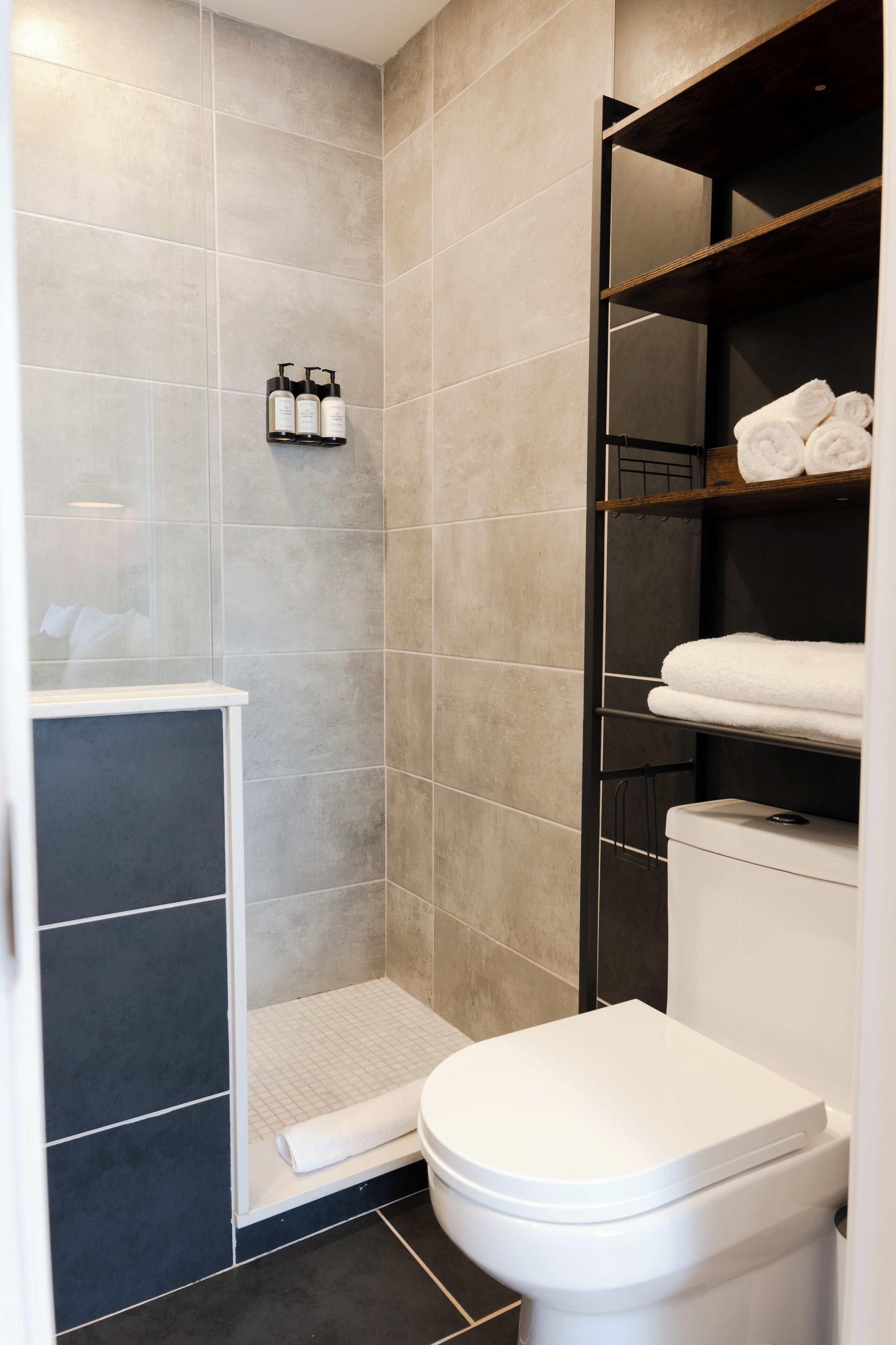 Ein modernes Badezimmer mit Dusche, Toilette und Handtüchern auf Regalen.