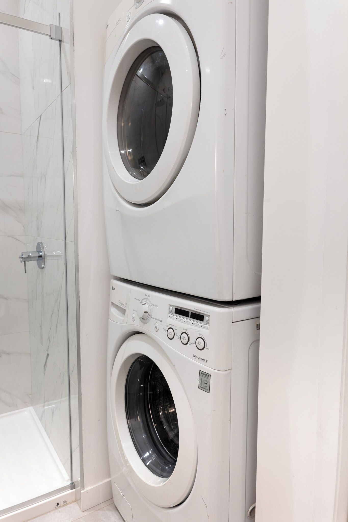 A stacked washer and dryer unit in a bathroom with a glass shower door.