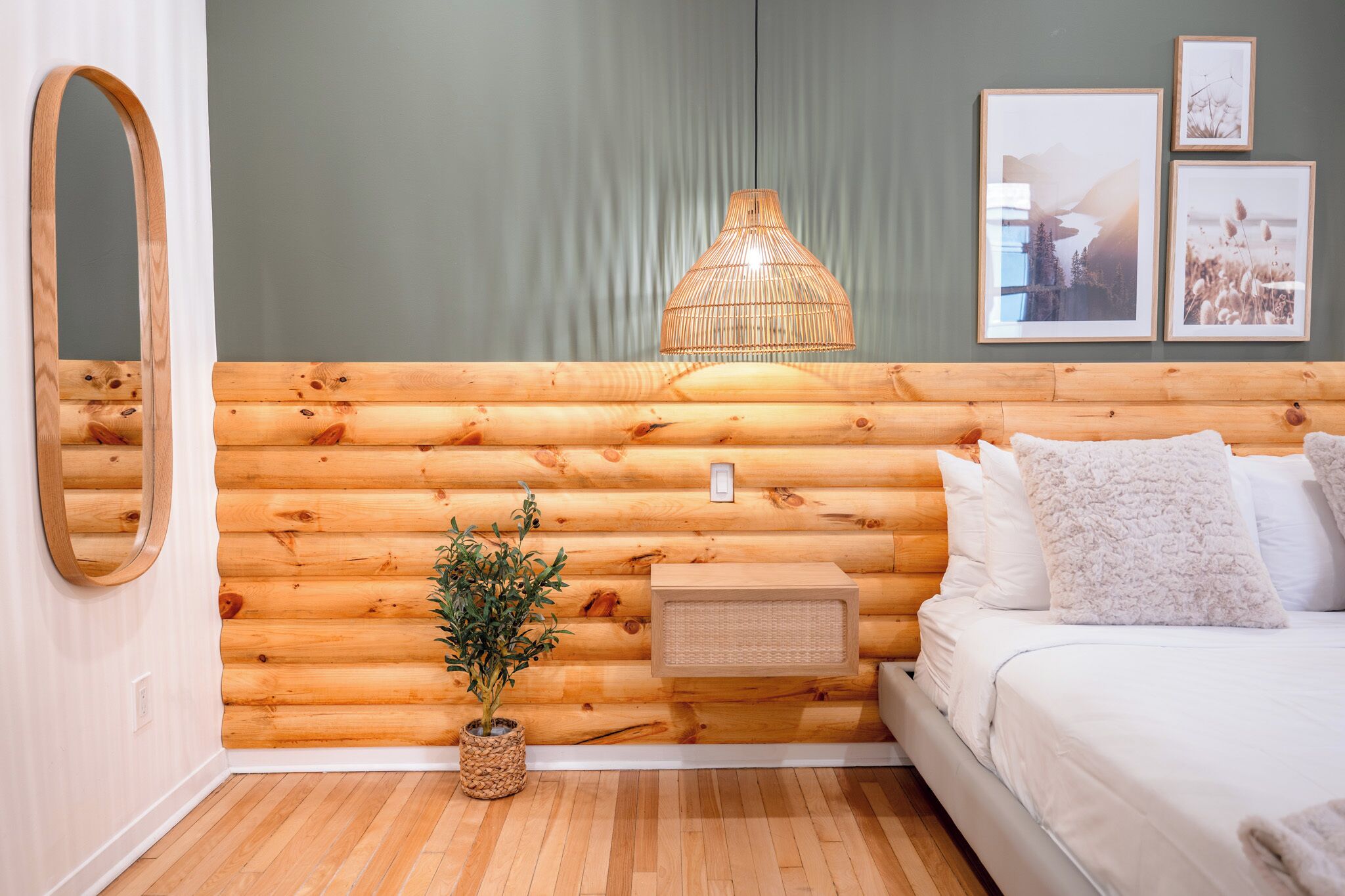 Une pièce aménagée dans le style d’un chalet en rondins, avec un lit, un luminaire suspendu, un miroir et des tableaux encadrés accrochés au mur.