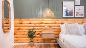 Une pièce aménagée dans le style d’un chalet en rondins, avec un lit, un luminaire suspendu, un miroir et des tableaux encadrés accrochés au mur.