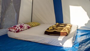 A tent with a bed, pillows, and a blanket.