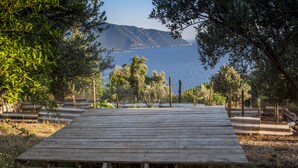 A wooden deck with a bench, surrounded by trees and overlooking a body of water with hills in the distance.