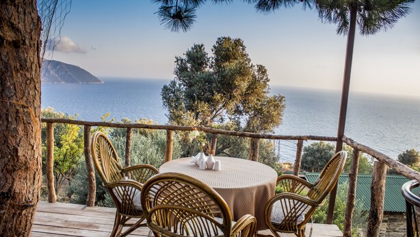 A wooden deck with wicker chairs and a table, overlooking a body of water and trees.