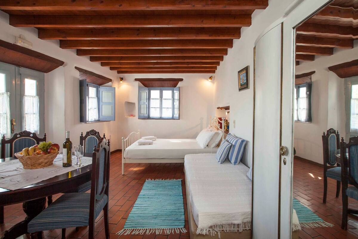 A cozy room with a bed, a sofa, a dining table with chairs, and a window.