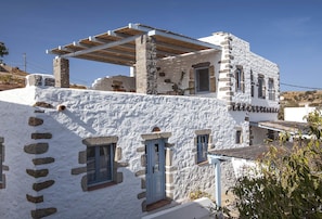 A traditional stone building with a white exterior, multiple windows, and a wooden pergola structure. - Theologos Houses (Patmos)