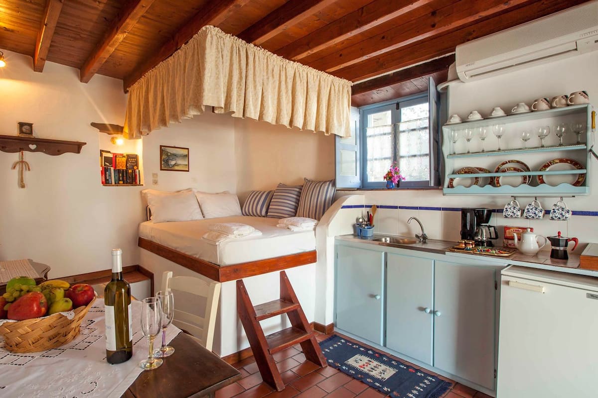 A cozy room with a loft bed, a small kitchen area, and a dining table with a basket of fruit and wine bottles.