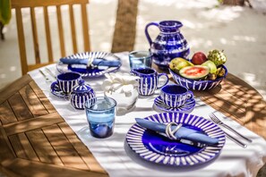 A round wooden table set with blue and white striped tableware, including plates, cups, and a pitcher, arranged on a white tablecloth.