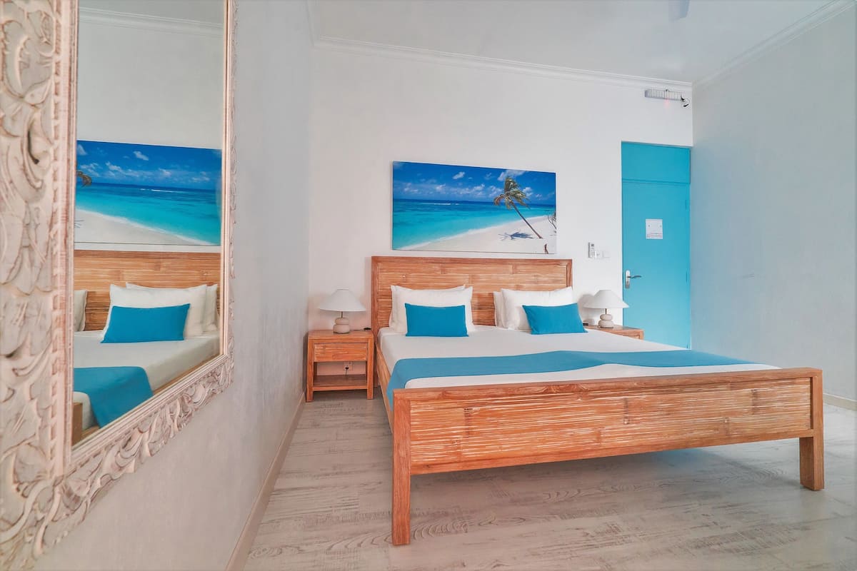 A bedroom with a wooden bed, a nightstand, a mirror, and a painting of a beach scene.