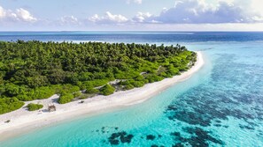 An aerial view of a tropical beach with clear turquoise waters, a sandy shoreline, and dense green vegetation.