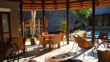 Un patio exterior con techo de paja, mobiliario de madera y una piscina.