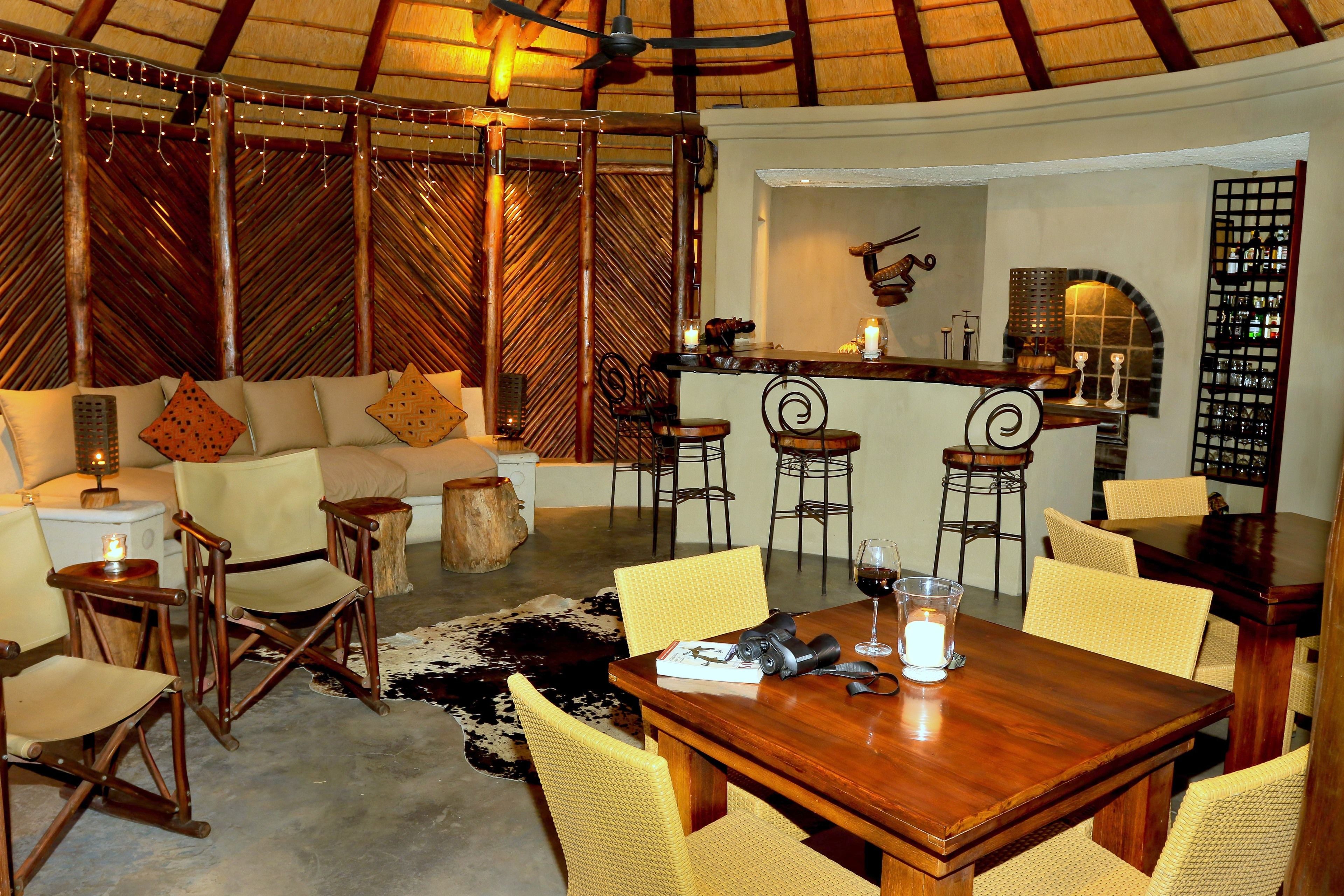 Un rincón tranquilo con una mesa de madera, sillas amarillas, un sofá con cojines estampados y una zona de bar con taburetes.