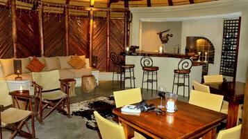 Un rincón tranquilo con una mesa de madera, sillas amarillas, un sofá con cojines estampados y una zona de bar con taburetes.