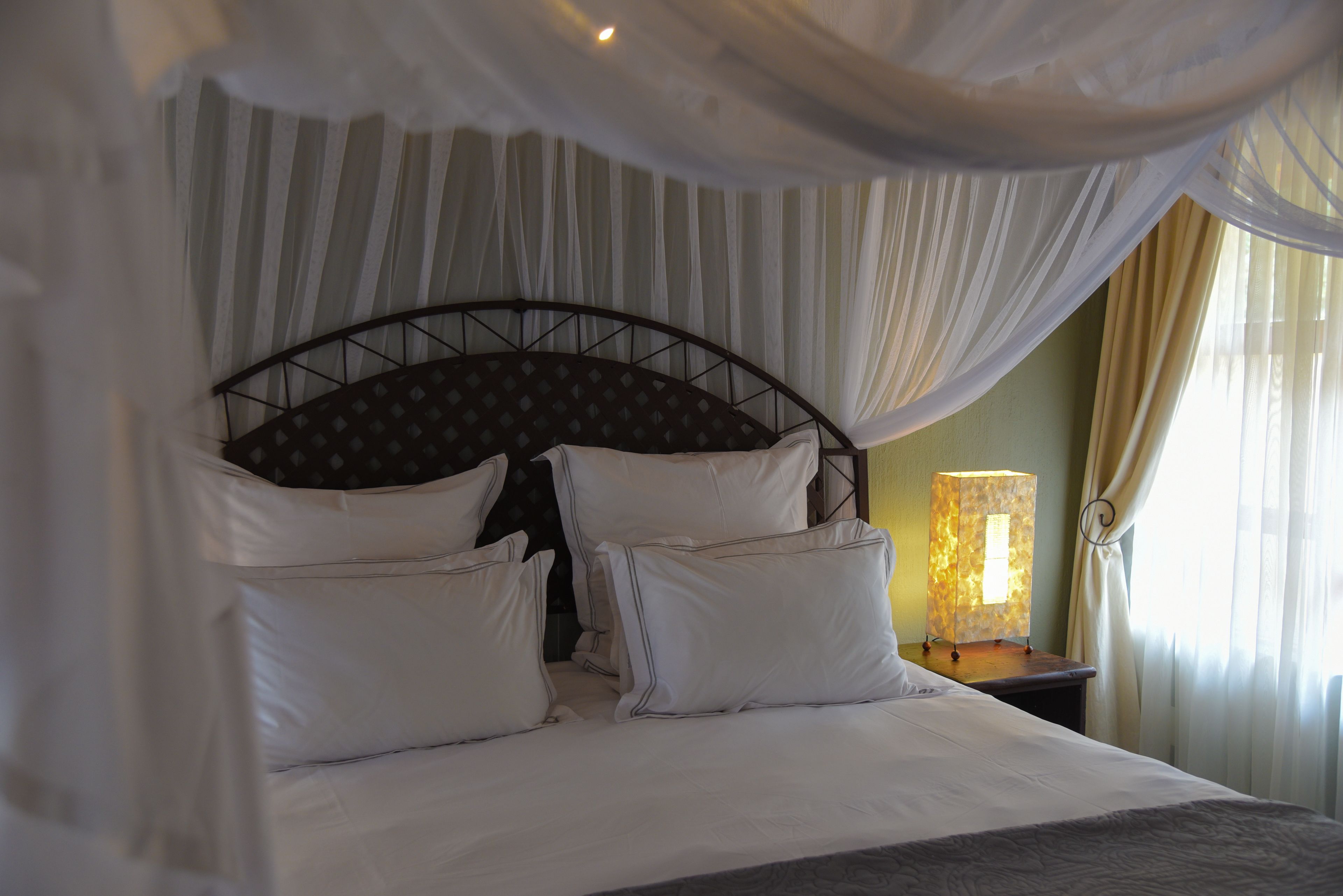 A bed with white bedding and a canopy, a nightstand with a lamp, and sheer curtains.