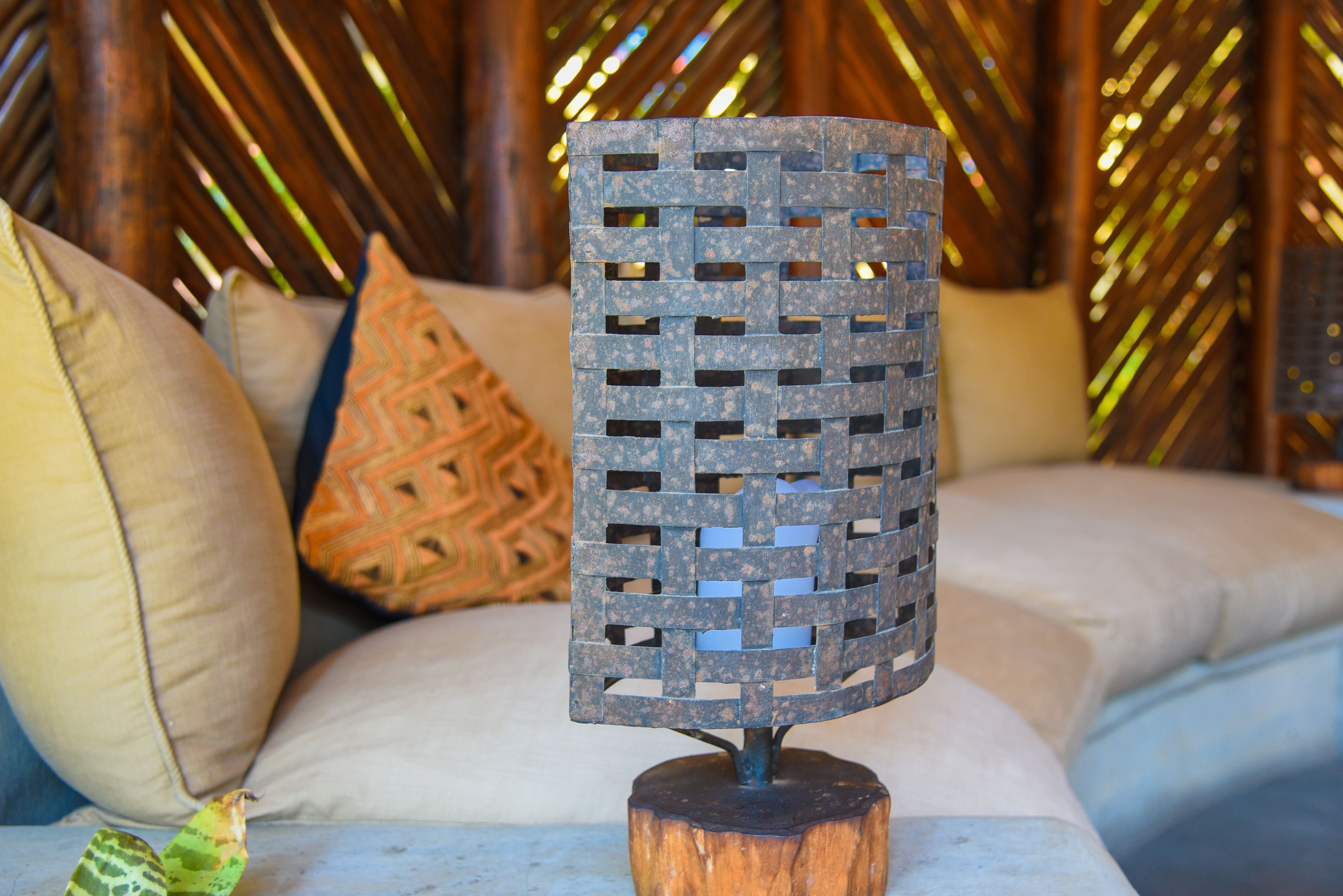 Eine dekorative Metalllampe auf einem Holzfuß, platziert auf einem Sofa mit gemusterten Kissen.