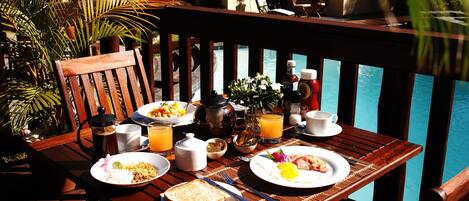A wooden table with breakfast items, a view of a pool, and a chair.