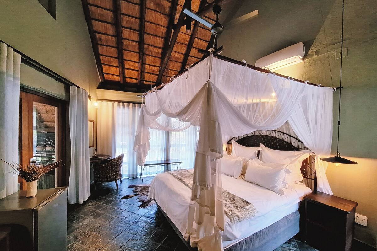 Un'ampia camera da letto con un letto grande, un baldacchino, una ventola a soffitto, un comodino e una finestra con tende.