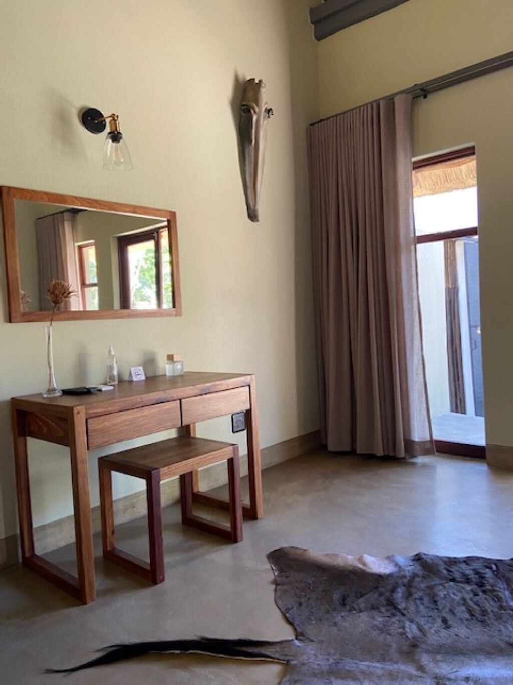 Une pièce avec un bureau en bois, un miroir, une fenêtre avec des rideaux et un grand tapis.