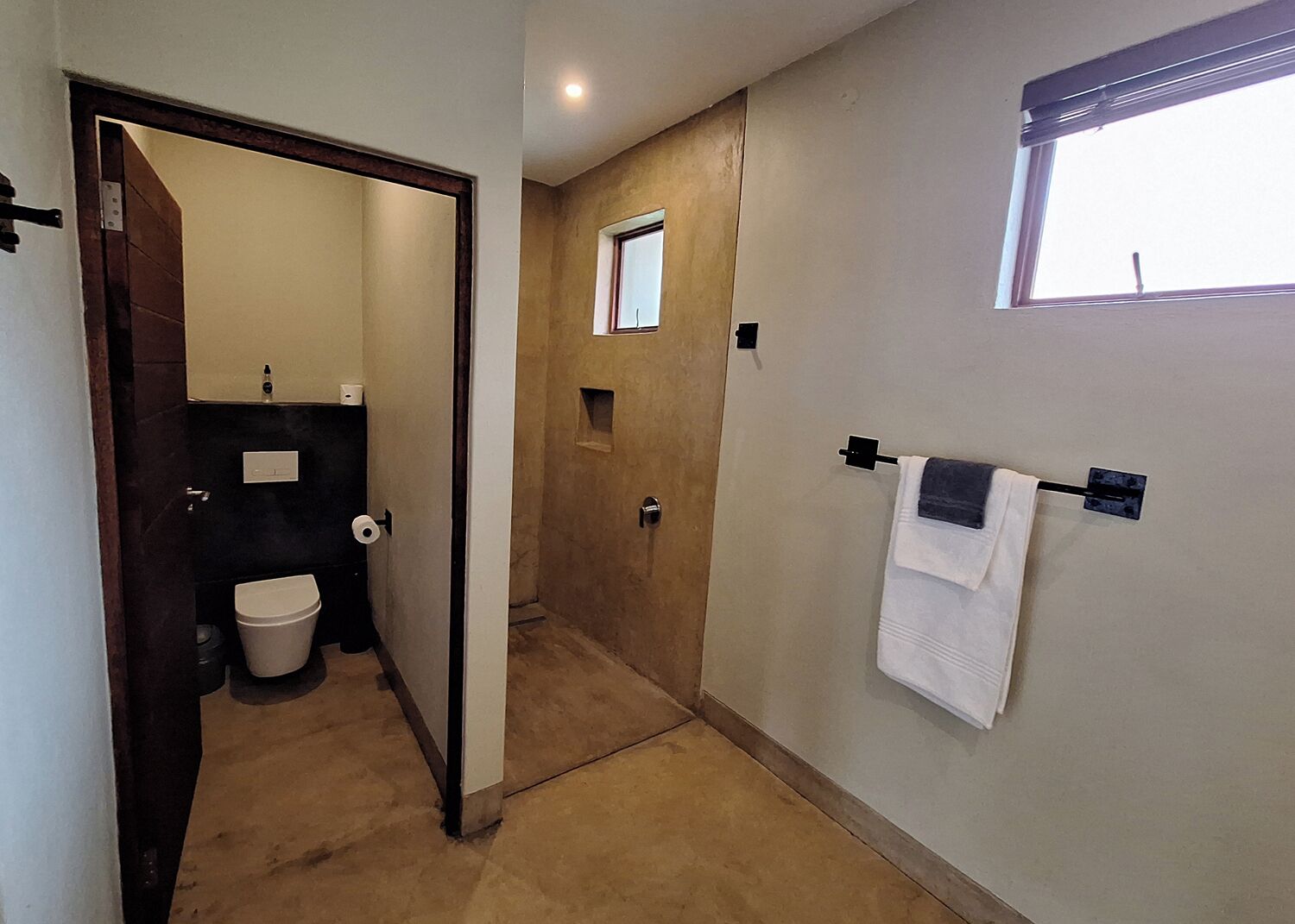 A narrow hallway with a wooden door, a small window, and a towel rack with a white towel.