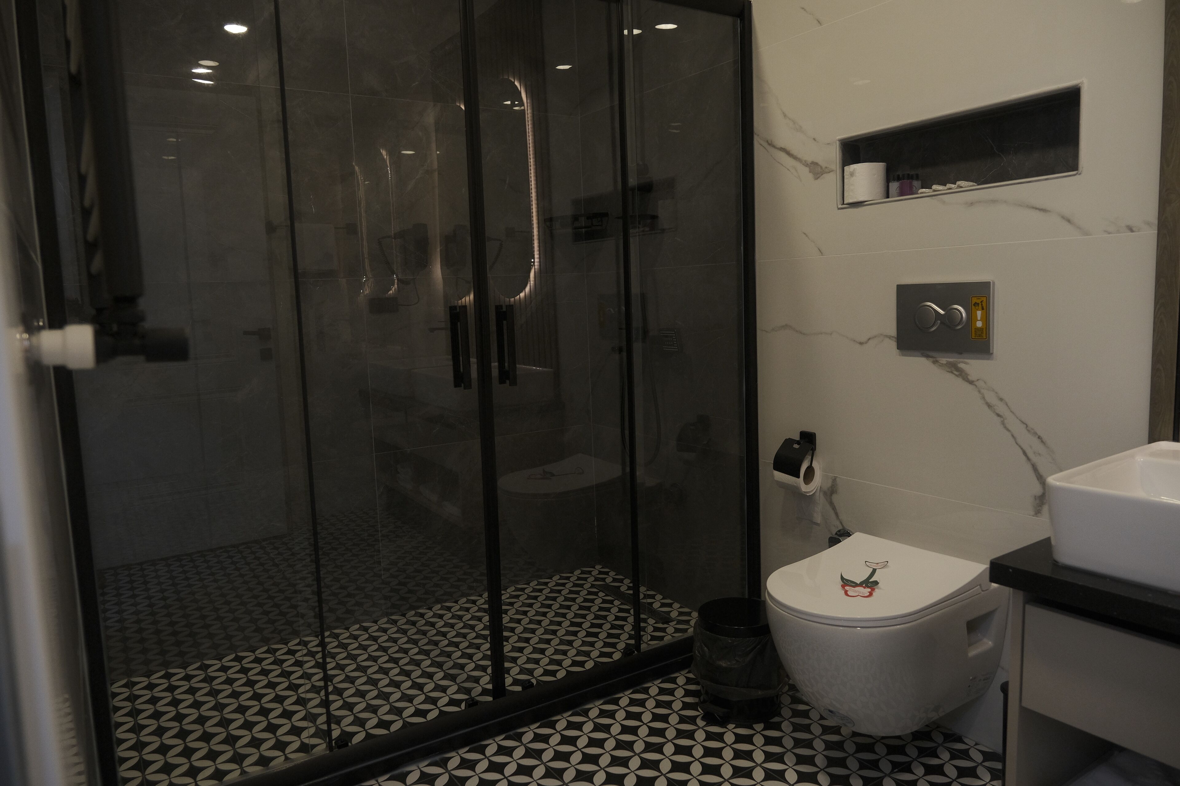 Un baño con ducha de vidrio, inodoro con tapa decorativa y salpicadero de mármol.