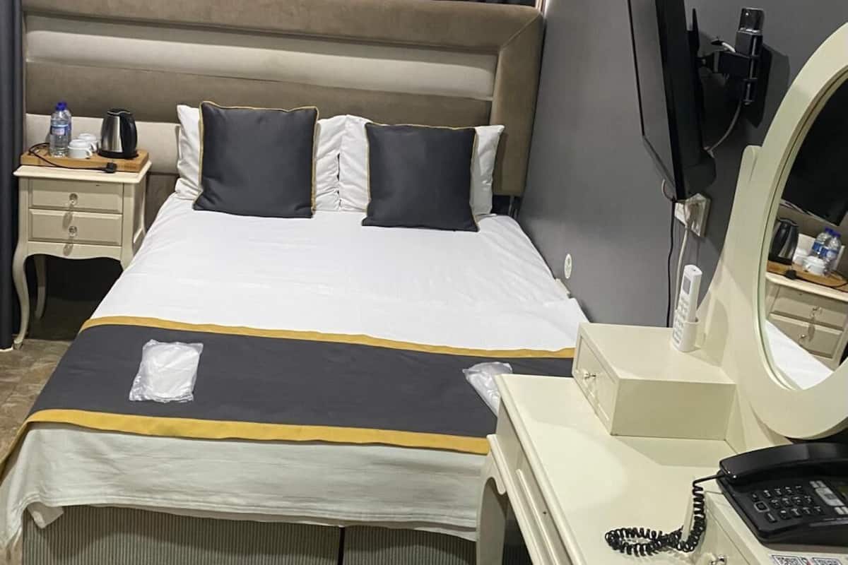 A hotel room with a bed, bedside table, and a desk with a telephone and a mirror.
