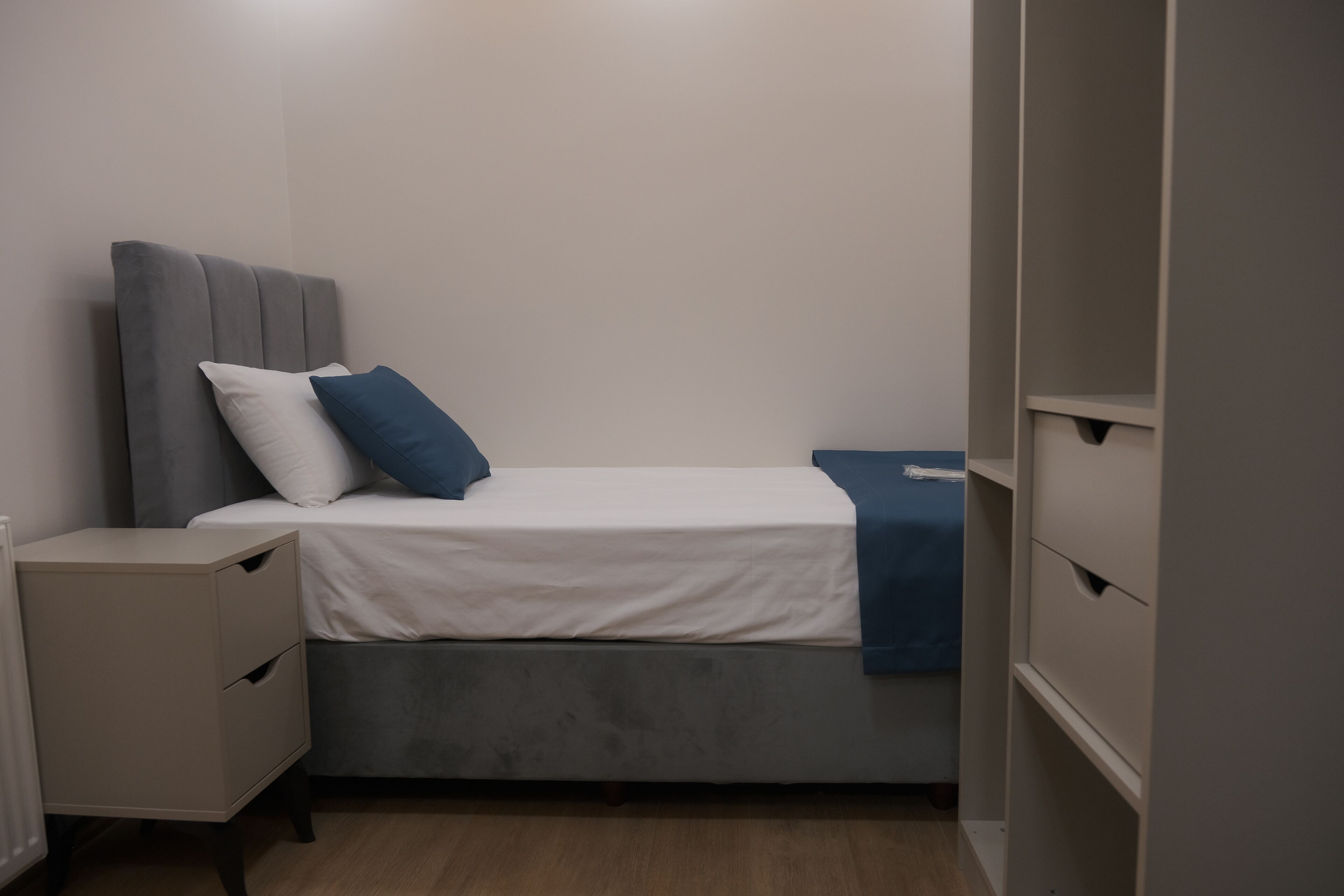 A small, neatly arranged bedroom with a single bed, a bedside table, and a wardrobe.