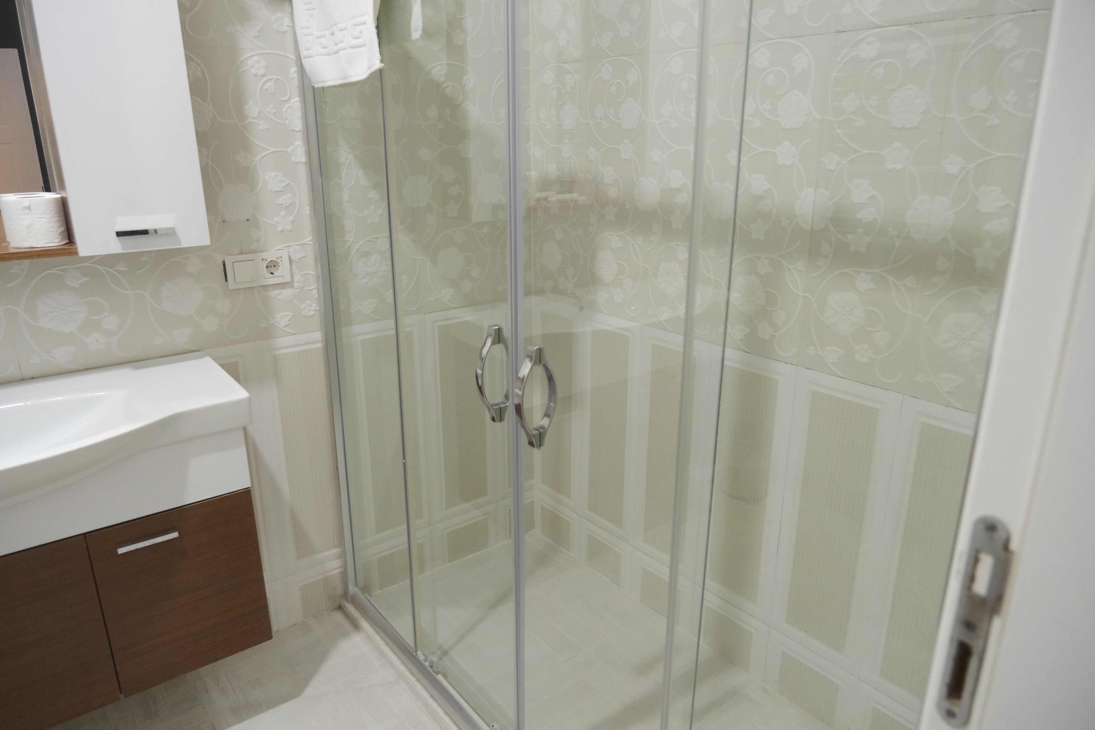 A bathroom with a glass shower enclosure, a white sink, and a wooden cabinet.