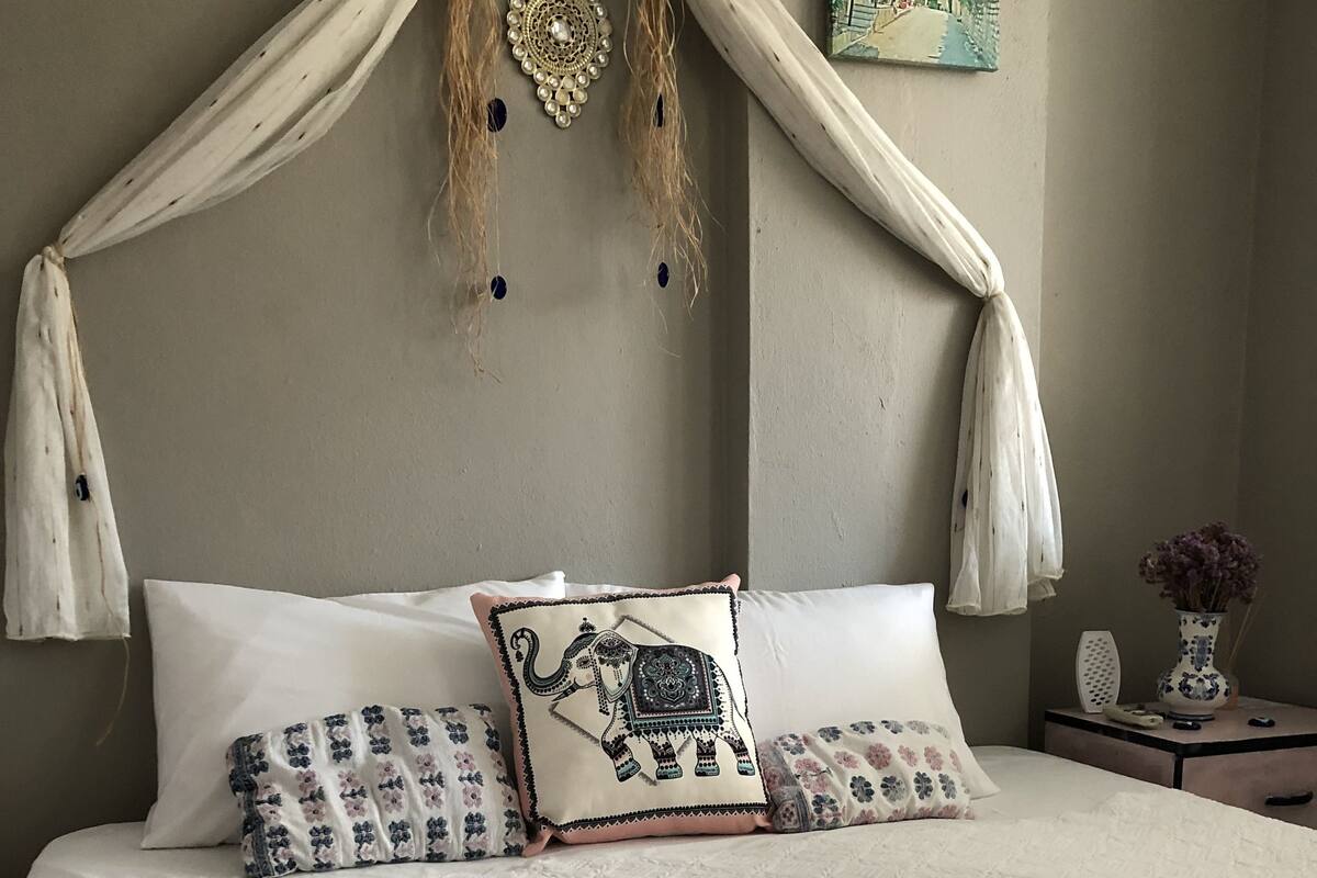 Una cama con dosel, varias almohadas, un jarrón con flores y un cuadro en la pared.