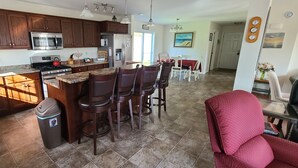 A kitchen with dark wooden cabinets, stainless steel appliances, and a granite countertop. There is a dining area with a red tablecloth and chairs. - A spacious sanctuary with 10+ private acres a few miles from Acadia NP entrance (Bar Harbor)