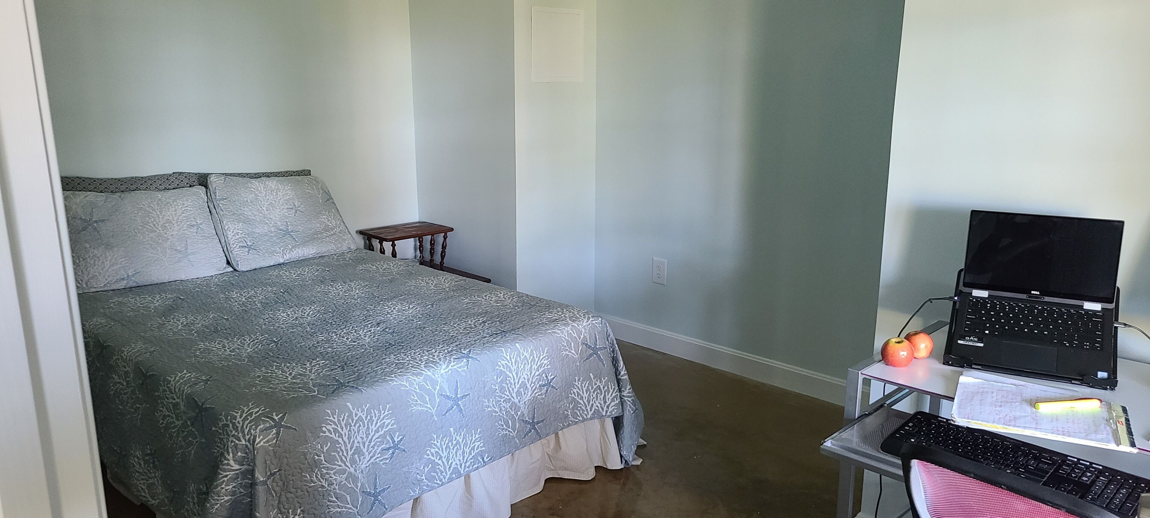 Une chambre à coucher avec un lit, une petite table de chevet, un ordinateur portable et une chaise.