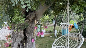Un jardín con una mecedora de macramé blanco, un árbol con flores rosas y una estructura de juegos infantiles.