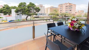 A balcony with a table and chairs, a flower vase, and a view of buildings and a body of water.