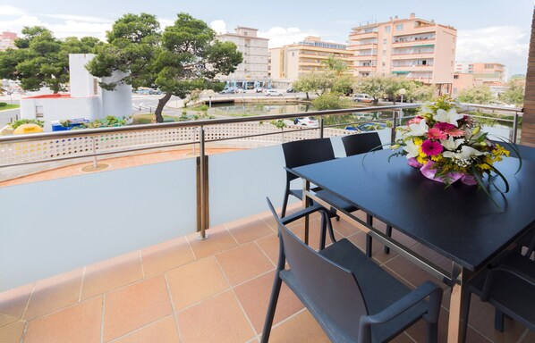 A balcony with a table and chairs, a flower vase, and a view of buildings and a body of water.