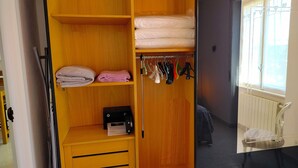 Puisesta valmistettu vaatekaappi, jossa on hyllyjä, henkaritanko ja pieni pöytä, jonka päällä on radio.