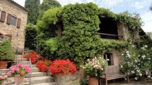 Un edificio de piedra con una escalera que lleva a una puerta, rodeado de abundante vegetación y plantas en flor.