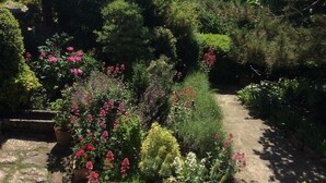Un jardín con diversas plantas y flores, un sendero de piedra y vistas a colinas distantes.