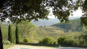 Una piscina con dos tumbonas, rodeada de vegetación y con vistas a un paisaje montañoso.