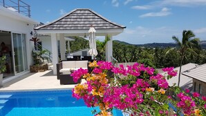 A modern outdoor pool area with a covered seating area, a clear view of the surrounding landscape, and vibrant bougainvillea flowers. - Villa Paradise with pool and sea view (Ko Samui)