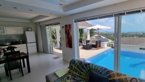 A modern living room with a large sliding glass door leading to a pool area. - Villa Paradise with pool and sea view (Ko Samui)