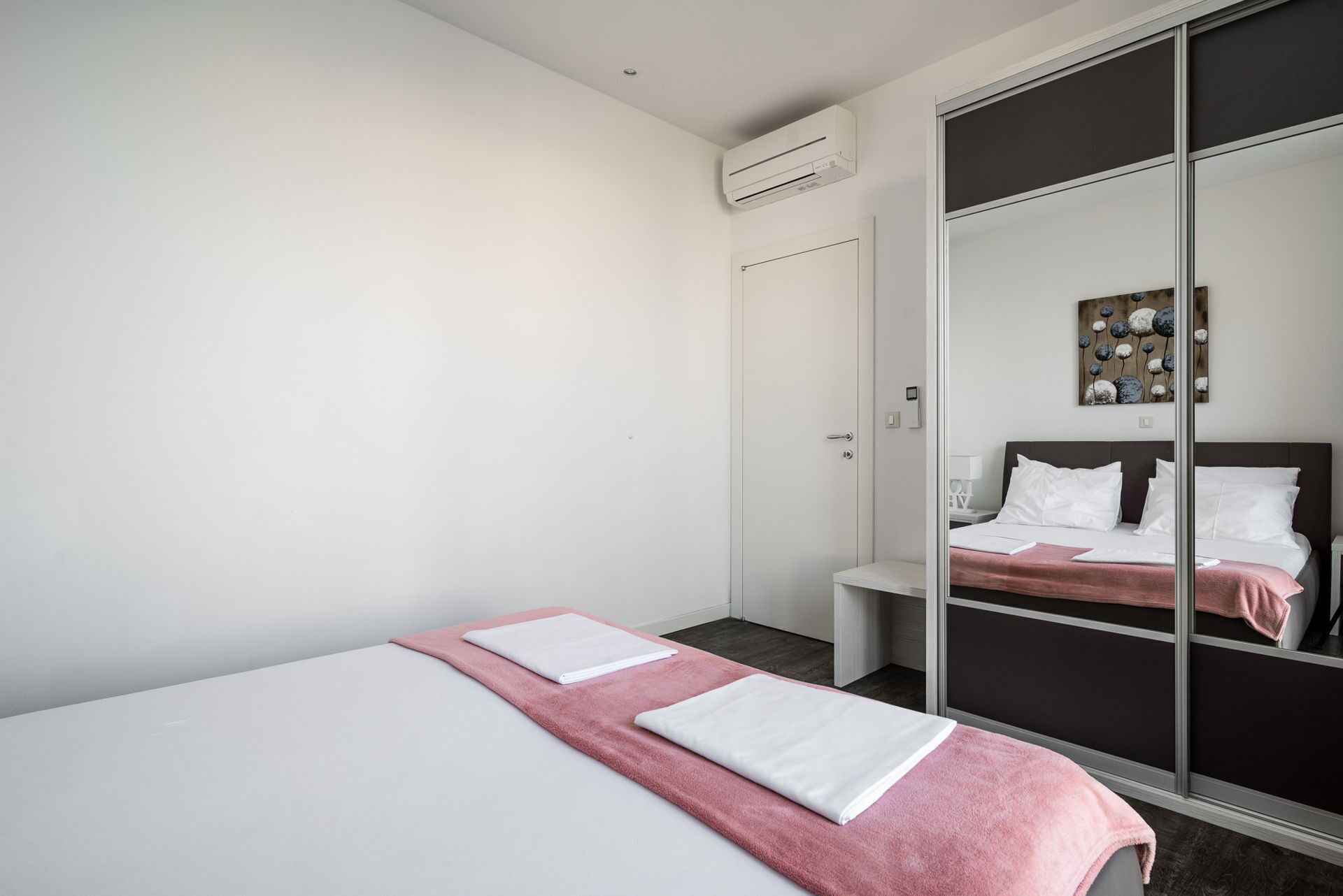 A hotel room with a bed, a wardrobe, and a bedside table.