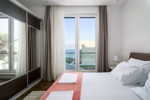 A hotel room with a bed, a nightstand, a window with curtains, and a view of the sea.